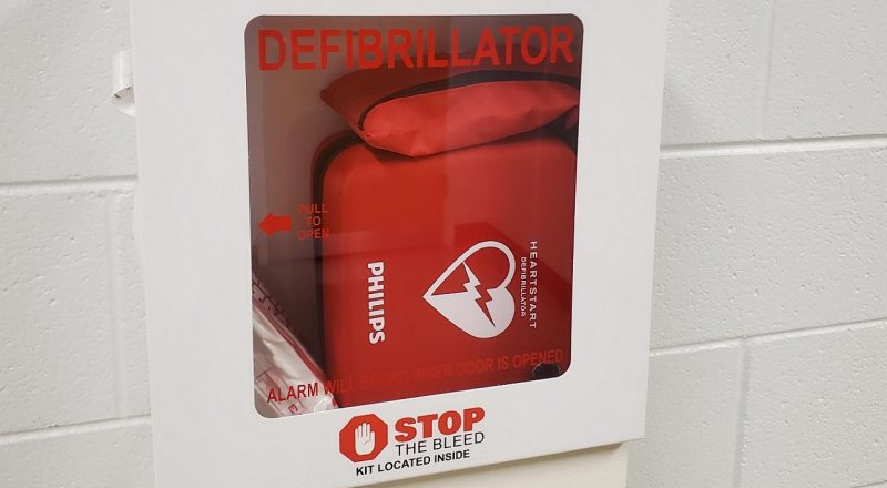 Red AED sitting in glass case on a white wall