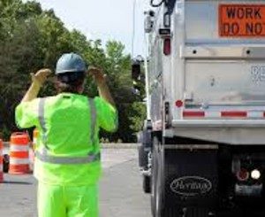Man wearing PPE guiding a dump truck backing up Man wearing PPE guiding a dump truck backing up