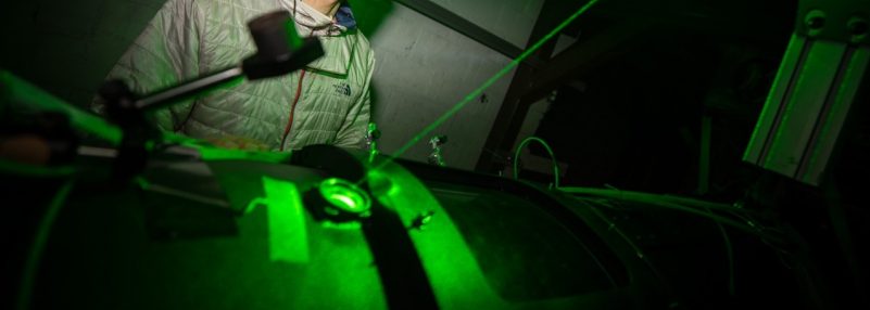Person standing in dark lab with bright green lasers